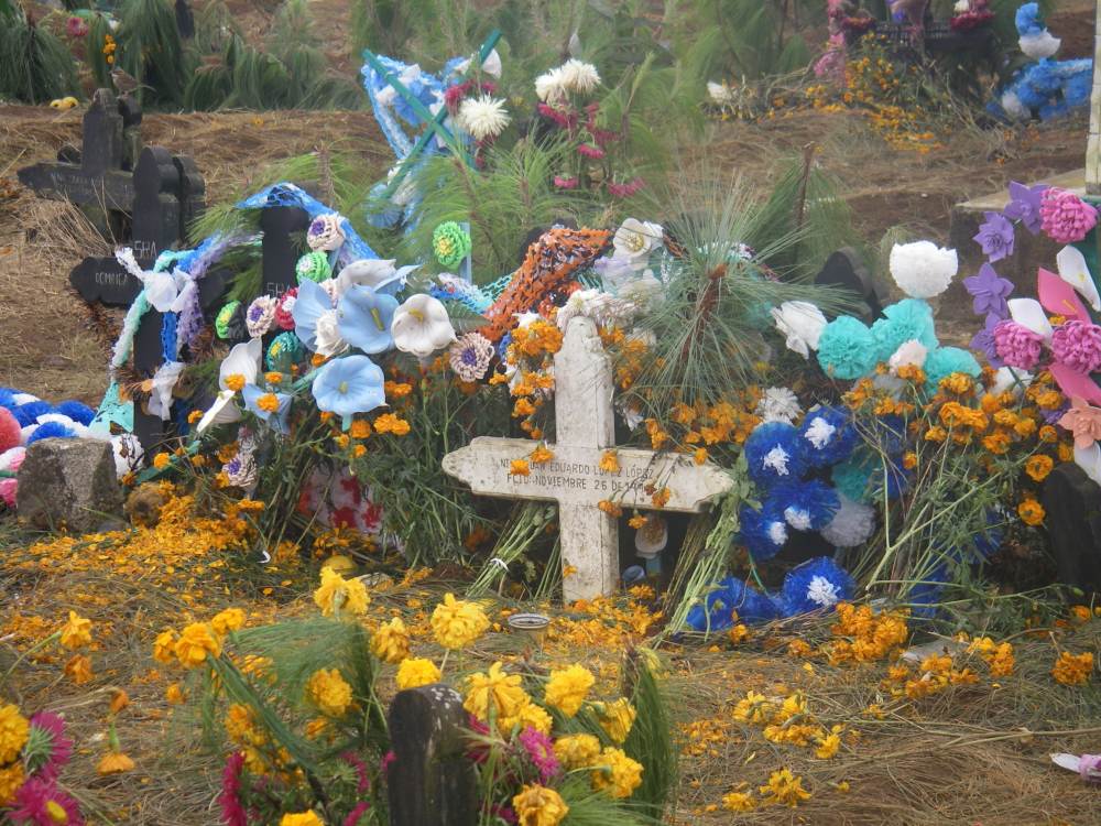 Grabkreuz umgeben von bunten Blumen.