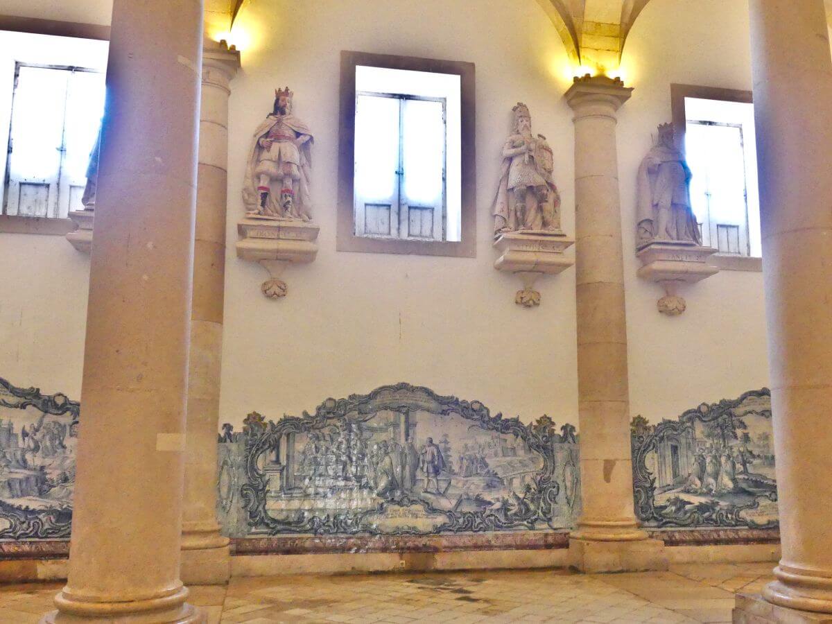 Saal mit Säulen, die Wände mit blauen Kachelbildern und Statuen geschmückt.