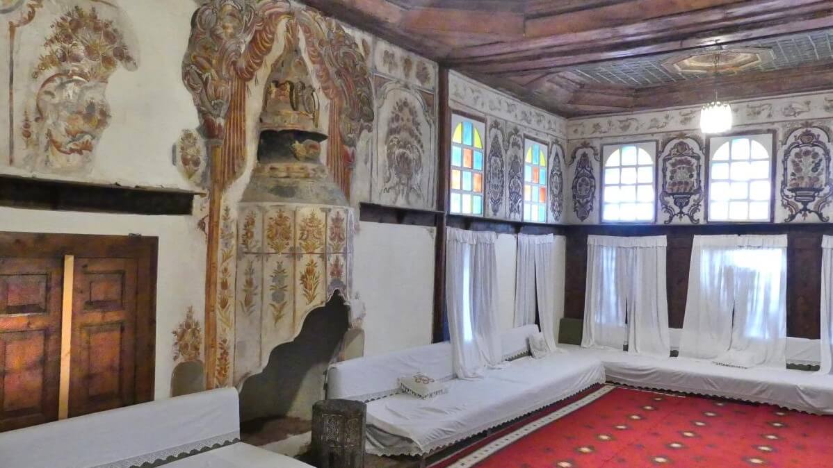 Raum mit rotem Teppich, Diwanen und Fresken an den Wänden.