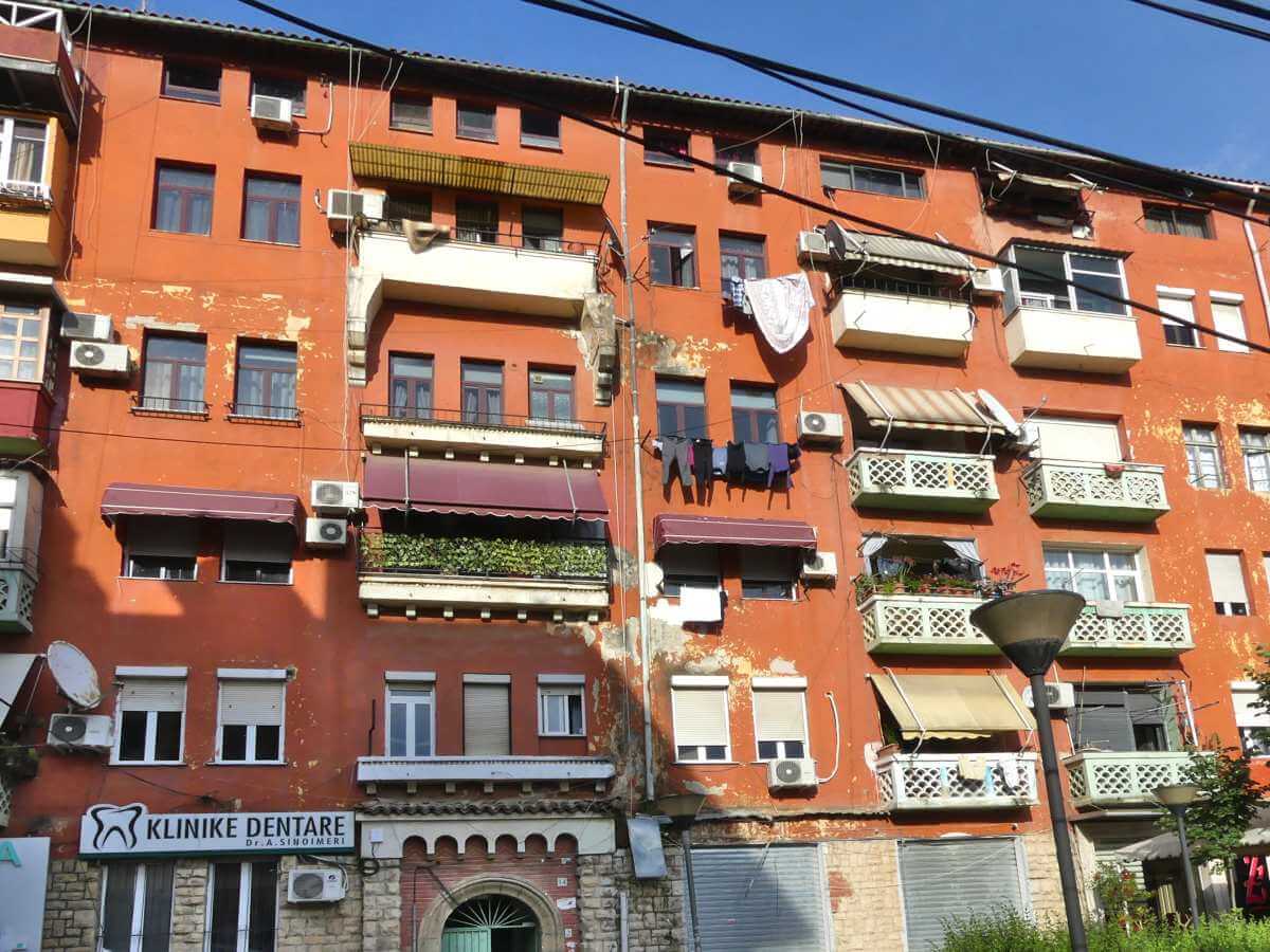 Fassade eines großen fünfstöckigen Hauses in Tirana, vor den Fenstern hängt Wäsche.