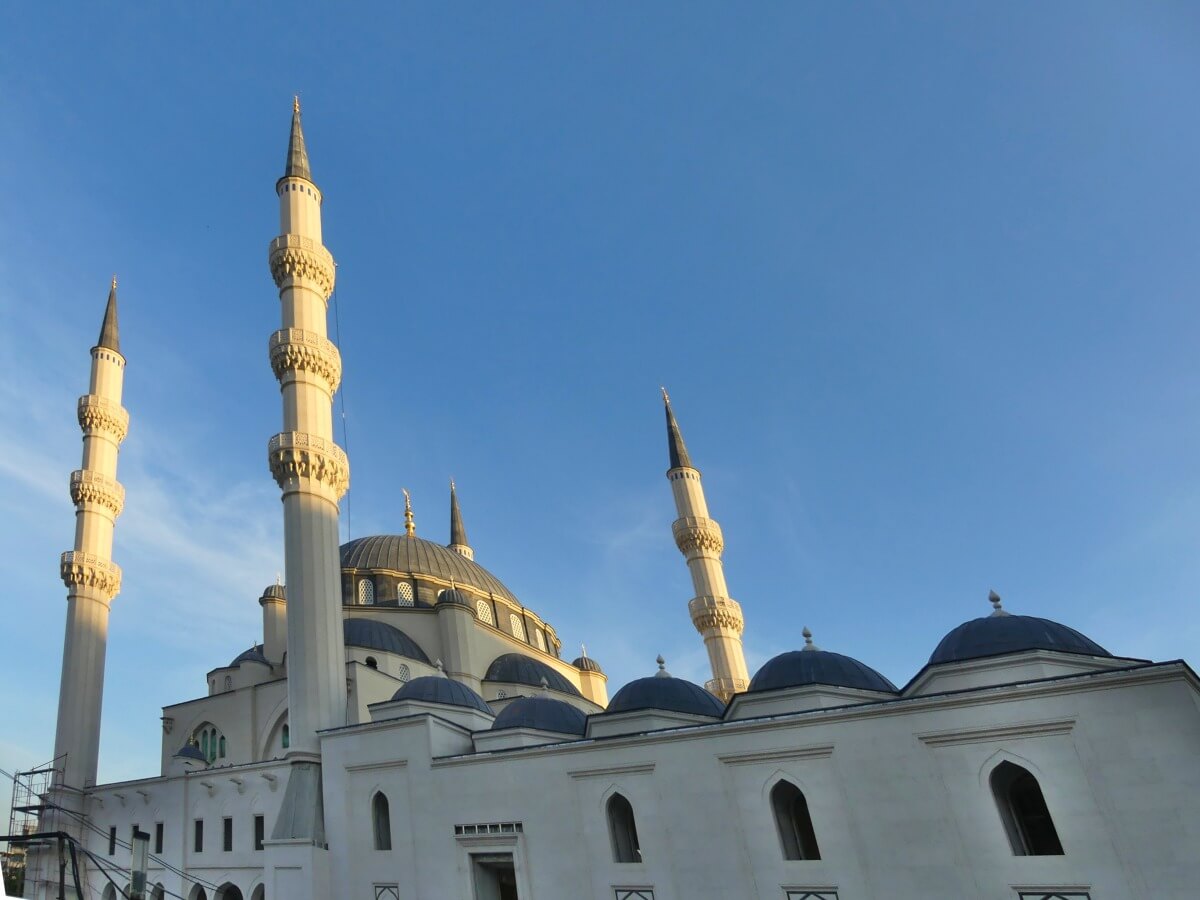 Moschee mit großem Kuppelbau und vier schlanken Minaretten vor blauem Himmel.