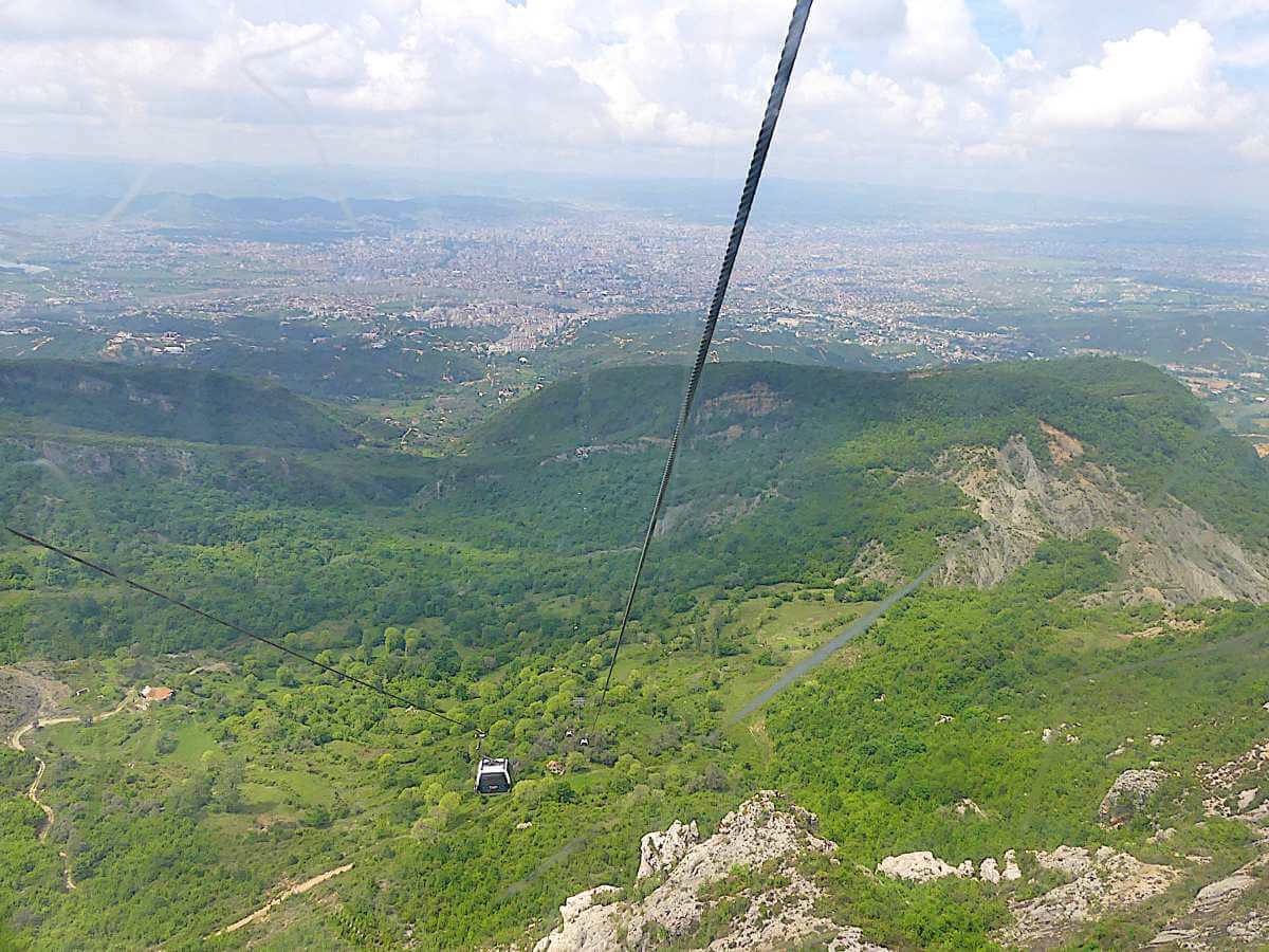 Blick aus der Höhe über steile grüne Hänge und den Talkessel von Tirana.