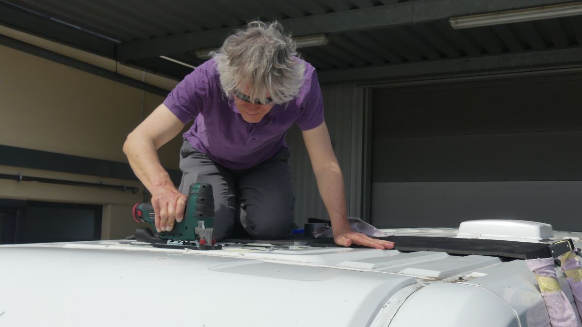 Marcus kniet auf dem Dach des Kastenwagens und sägt die Öffnung für die Dachluke.