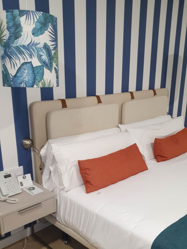 Hotelzimmer mit blau-weiß gestreifter Wand und Doppelbett.