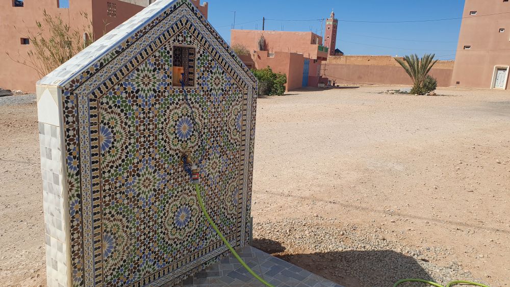 Mit Mosaiken verzierte öffentliche Wasserstelle mit Wasserhahn zum Entnehmen.