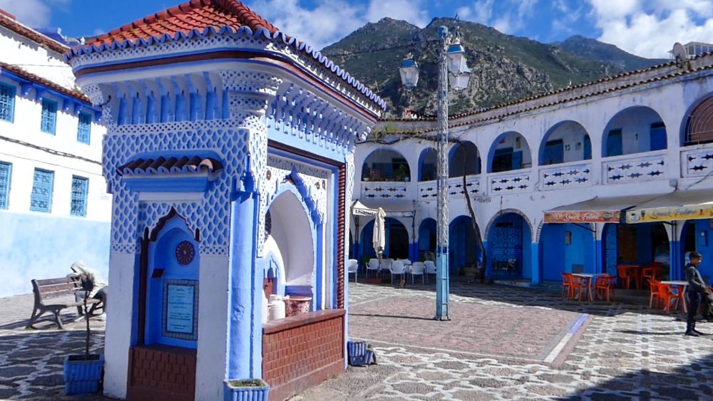 Ein Platz mit blau-weiß gestrichenen Gebäuden ringsum, in der Mitte ein orientalisch verzierter blau-weißer Brunnen.