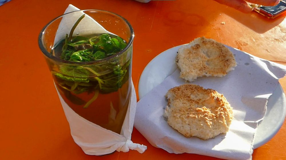 Oranger Tisch, auf dem ein Glas mit Minztee und ein Teller mit Gebäck stehen.