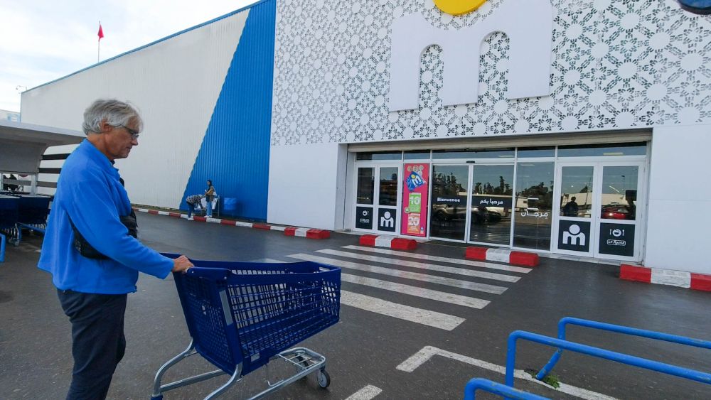 Marcus schiebt einen Einkaufswagen auf den Eingang des großen Marjane-Supermarkts zu.