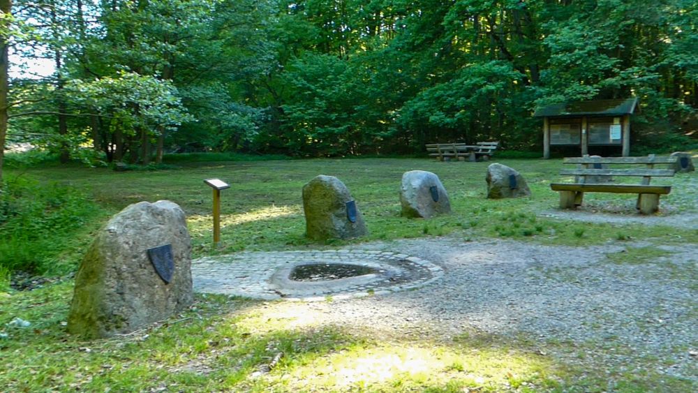 Steinbecken im Boden, ringsum große Steine aufgereiht.