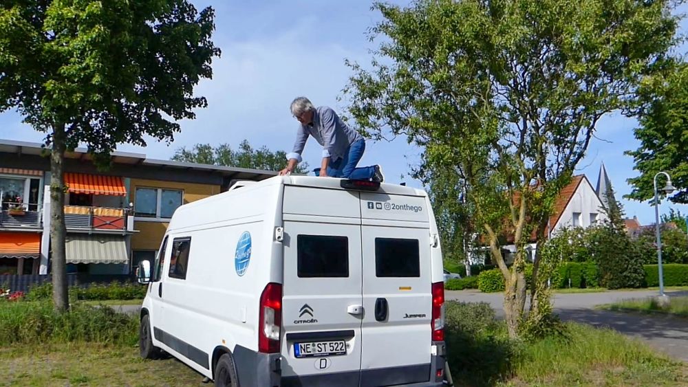 Marcus kniet auf dem Dach des Vans und putzt ihn.