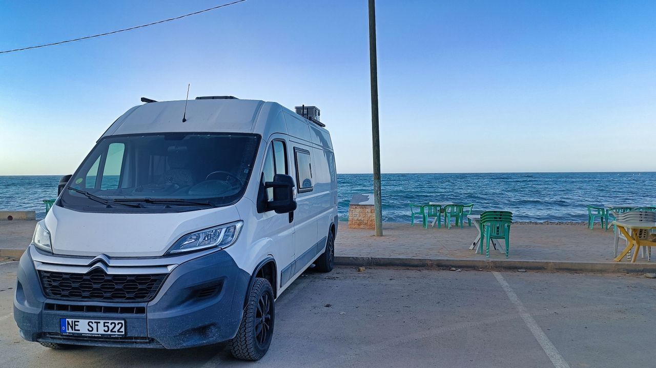 Wohnmobil steht auf einem Parkplatz am Meer.