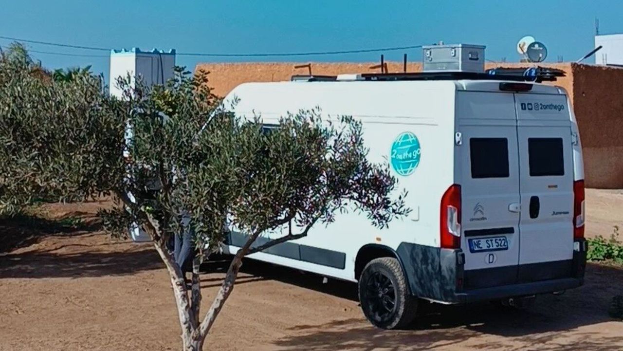 Wohnmobil auf dem Campingplatz. Der Boden ist rötlich, im Vordergrund ein kleines Bäumchen.