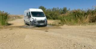 Wohnmobil fährt durch eine kleine Furt, Wasser spritzt unter den Vorderrädern.